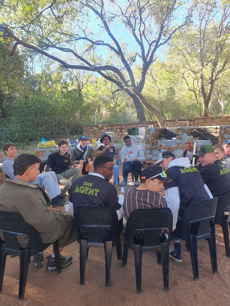 Boys and leaders sitting in a circle under trees during a camp talk